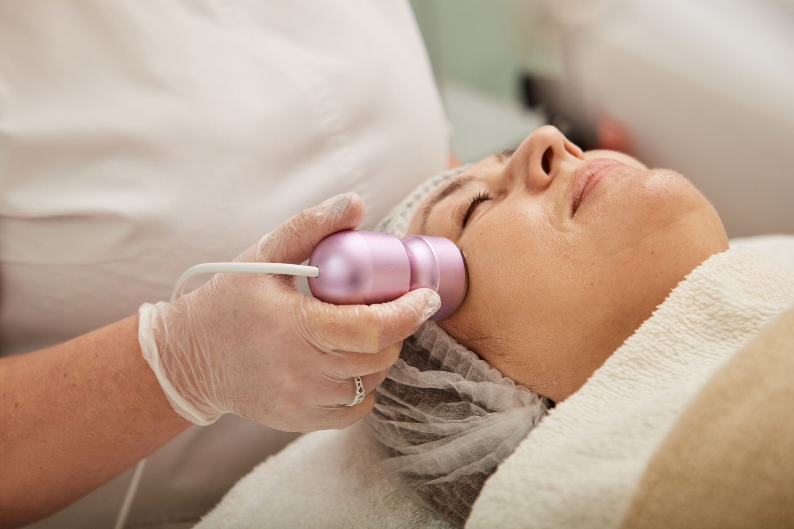 Close up of beautician hand in glove using professional cosmetic device while performing anti-aging skincare procedure