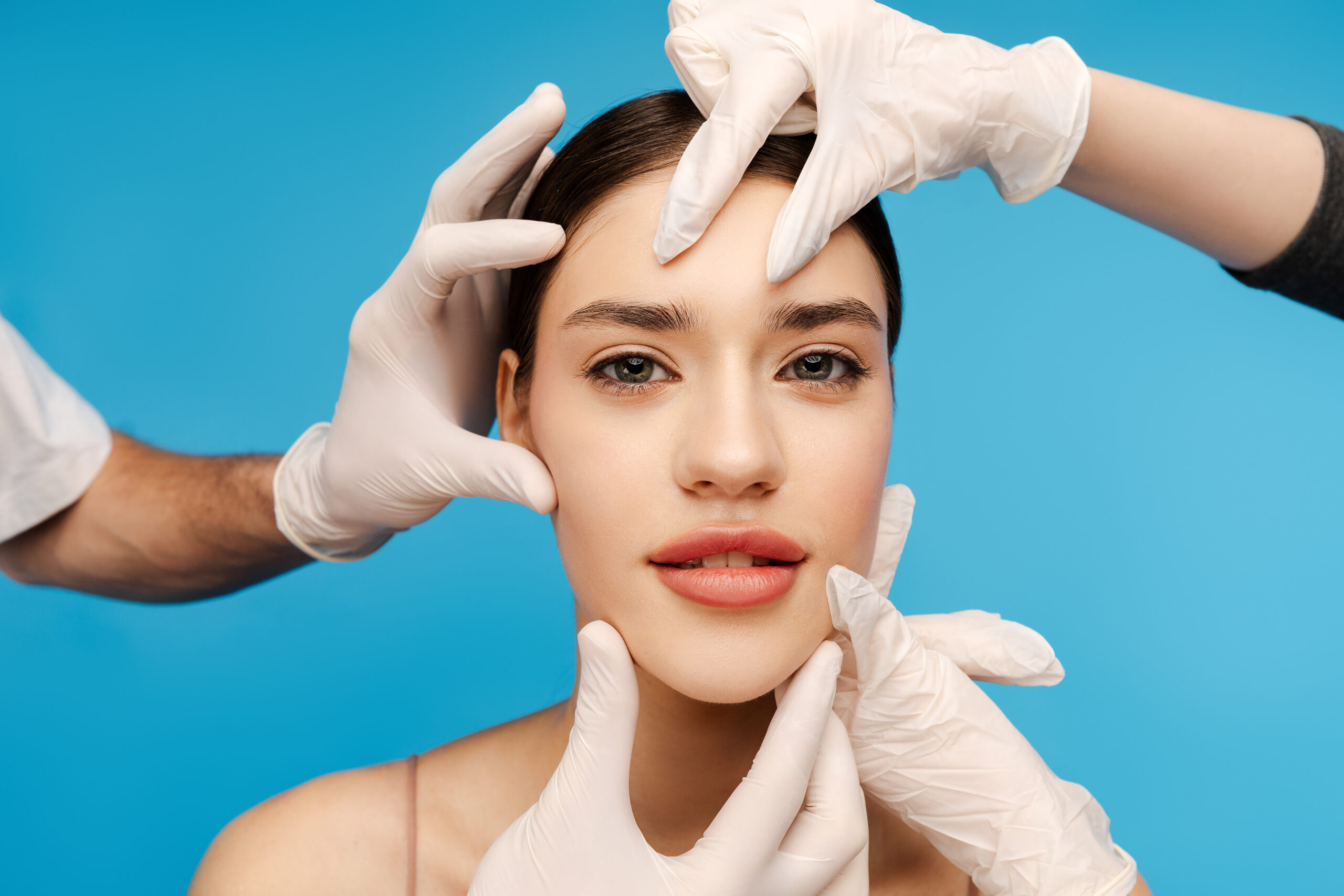 Cosmetologist doctor making botox injection for young woman. Isolated on blue background. Beauty care, anti aging procedures, plastic surgery concept